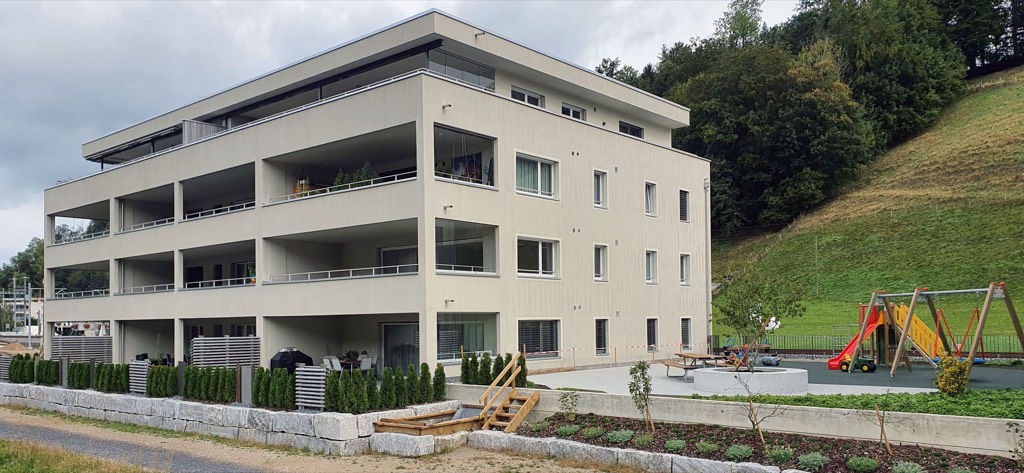 Aussenansicht eines Hauses der Überbauung Birkenweg mit Spielplatz und Sitzplatz im Vordergrund.