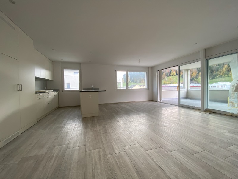 Offener Wohn- und Essbereich mit Küchenzeile, Kochinsel und bodentiefen Fenstern zum Balkon.