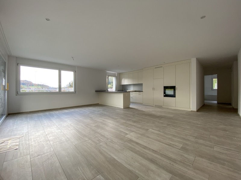 Wohnzimmer mit breitem Panoramafenster und angrenzender Küche mit Backofen und Kochinsel.