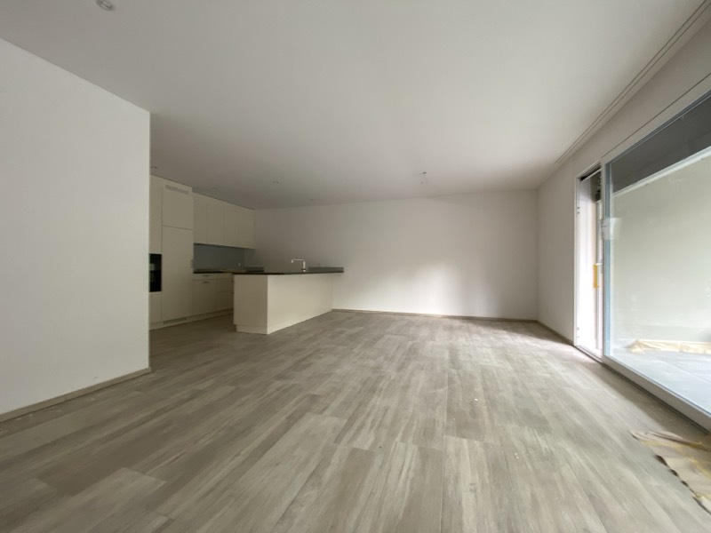 Heller Wohnraum mit Küchenzeile und raumhoher Schiebetür zum Balkon.